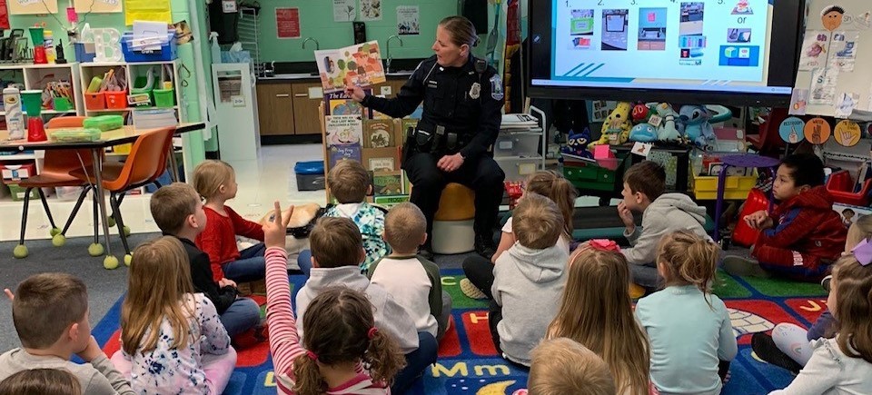 police officer reading a book to elementary students